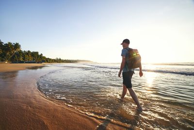 Solo traveler walking on empty beach. rear view of man with backpack at sunrise. 