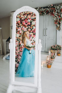 Young woman wearing blue dress reflecting in mirror against flowering plants