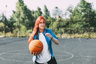 A young basketball player is training on an outdoor basketball court, a teenage girl is playing