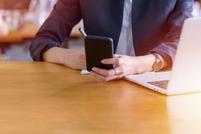 Midsection of man using mobile phone while sitting on table