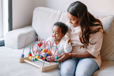 Happy smiling mixed race indian mother and african black baby toddler playing wooden bead maze toy 