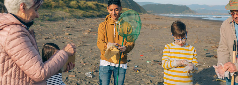 Grandparents and grandchildren putting on protective gloves while standing at beach