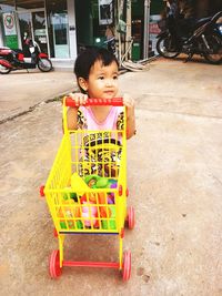 High angle view of cute girl with toys in shopping cart standing on footpath