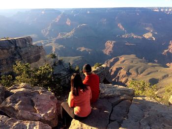 Rear view of couple sitting on rock against mountain