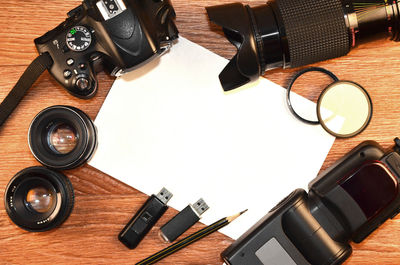 Directly above shot of modern camera and blank paper on wooden table