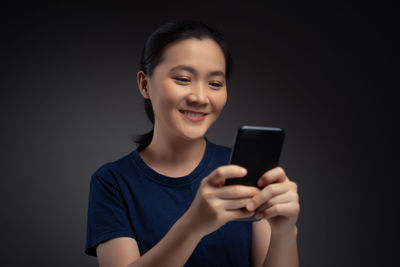 Portrait of smiling man holding mobile phone against black background