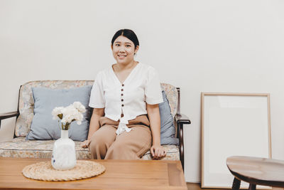 Portrait of smiling young woman sitting on table at home