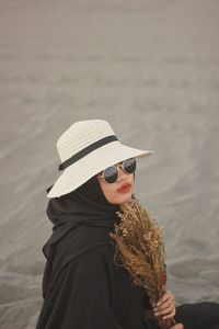 Side view of woman wearing hat and sunglasses sitting at beach