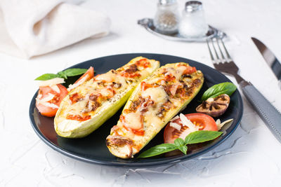 Ready-to-eat baked zucchini halves filled with cheese and tomato and basil leaves on a black plate