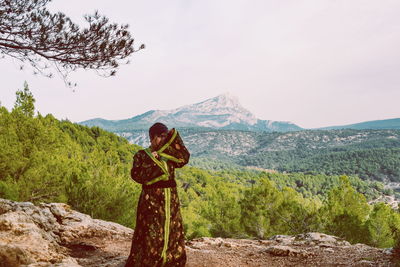 Woman wearing kimono while standing on mountain against sky