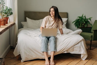 Young professional woman in t-shirt and jeans works remotely on computer from home