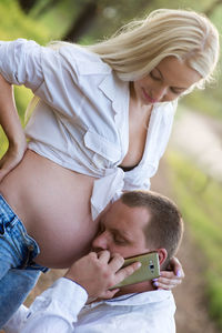 Man using mobile phone while to pregnant woman abdomen