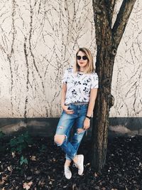 Portrait of young woman standing on tree trunk