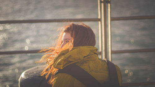 Rear view of half turned female in yellow jacket at sunset near sea