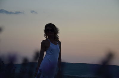 Young woman standing on land against sky during sunset