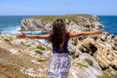 Rear view of woman standing on coast with her arms outstretched