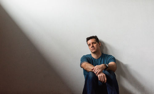 Portrait of tired man leaning against white wall with his eyes closed.