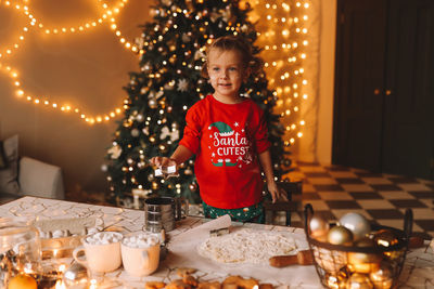 A little girl in red pajamas cooks and eats christmas cookies in the decorated kitchen of the house