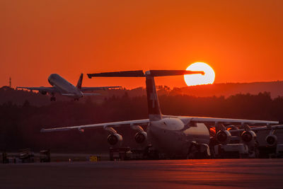 Airplane at runway against orange sky