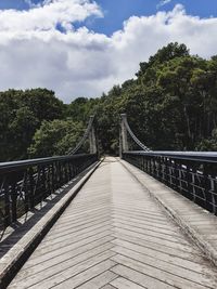 Footbridge amidst trees against sky