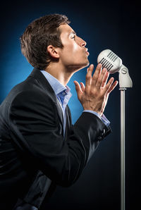 Young man making a face while singing against black background