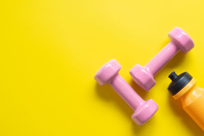 Directly above shot of dumbbells and water bottle on yellow background