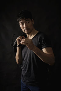 Young man looking away while standing against black background