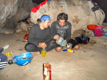 Friends preparing food while sitting against rocks at campsite