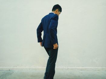 Side view of young man in suit standing against wall