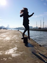 Silhouette young woman jumping on walkway by river