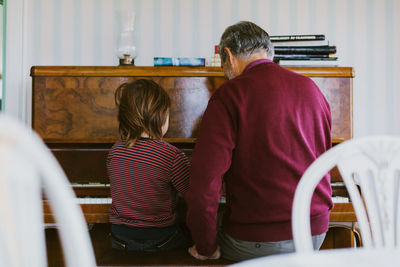 Rear view of boy playing piano with great grandfather at home