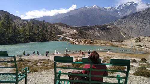 People sitting on bench by mountain against sky