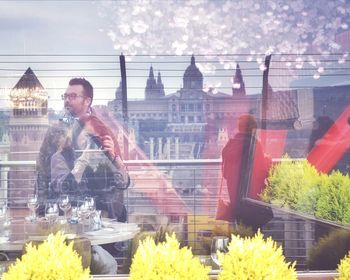 Man standing by window in city against sky