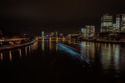 Illuminated bridge over river by buildings against sky at night