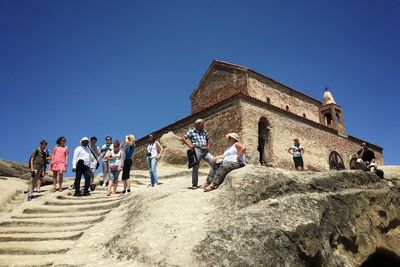 Low angle view of tourist at uplistsikhe cave against clear blue sky