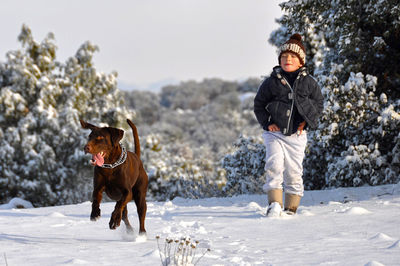 Boy walking with dog on snow covered field