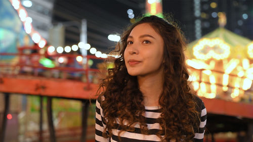 Portrait of young woman standing against illuminated light at night