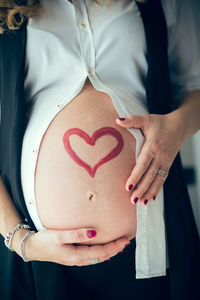 Midsection of pregnant woman touching abdomen with heart shape