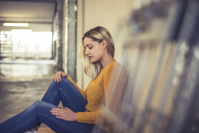 Young woman looking away while sitting in corridor