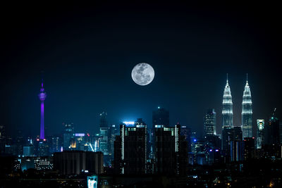 Full moon over illuminated modern cityscape at night