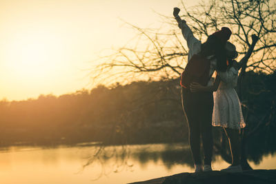 Rear view of mother with daughter standing by lake during sunset