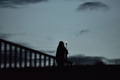 Rear view of woman standing against sky at dusk