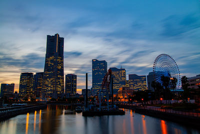 Illuminated buildings by river against sky in yokohama city