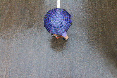 A minimalistic aerial view of a person in umbrella walking over the wet road on a rainy day .