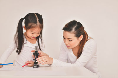 Woman adjusting microscope on table against wall