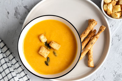 Top view of pumpkin, carrot cream soup in a bowl. with croutons, pumpkin seeds and bread sticks