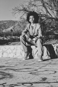 Full length portrait of boy sitting against tree on retaining wall