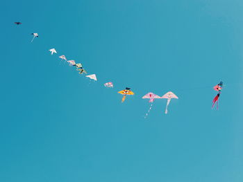 Low angle view of kites against clear blue sky