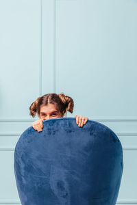 Teen girl hidden and happy in a blue armchair on turquoise background