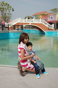 Side view of mother with cute son sitting by lake